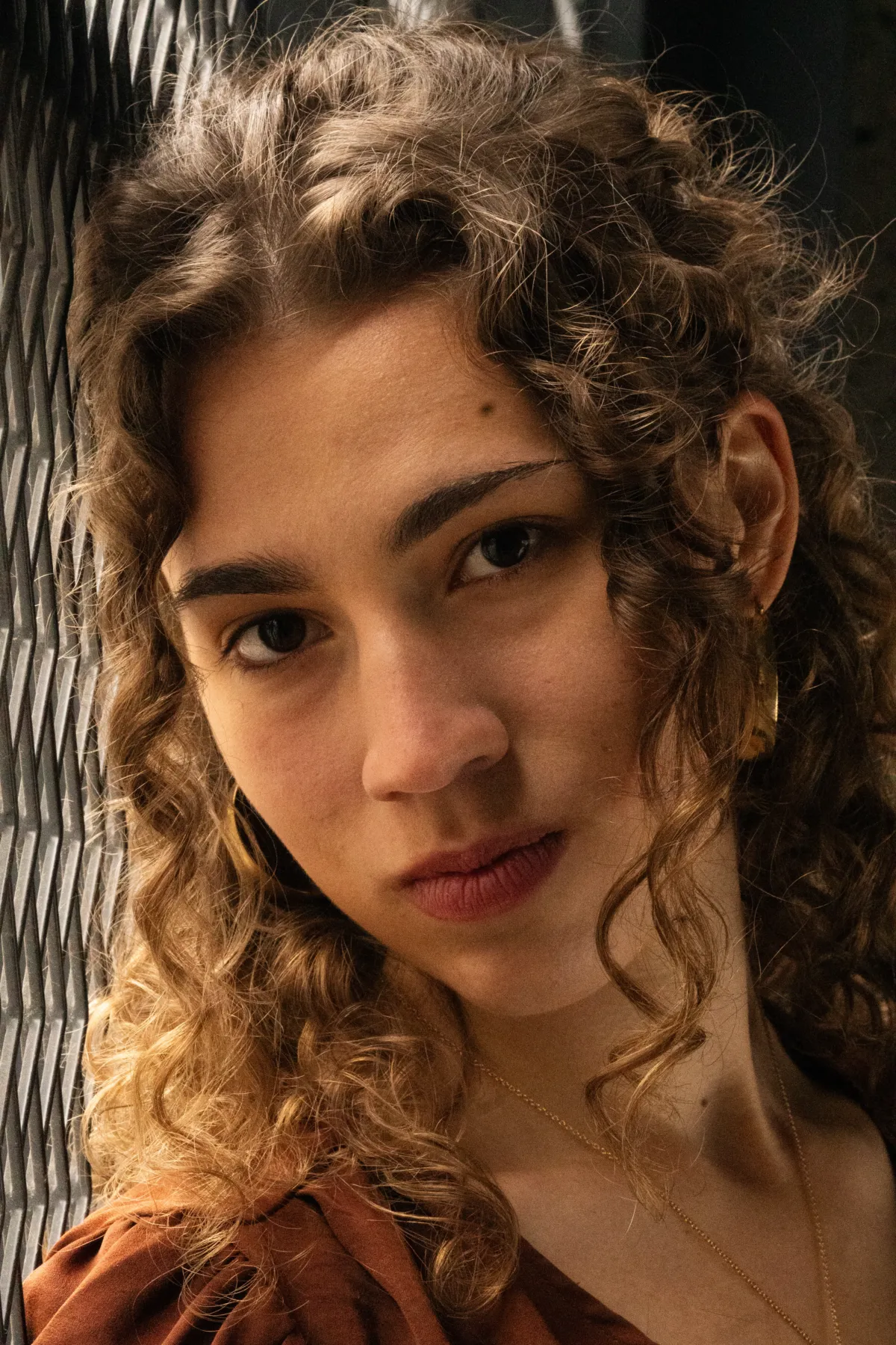 Nahaufnahme einer jungen Frau mit Locken, das Gesicht leicht geneigt, seitlich von warmem Licht getroffen