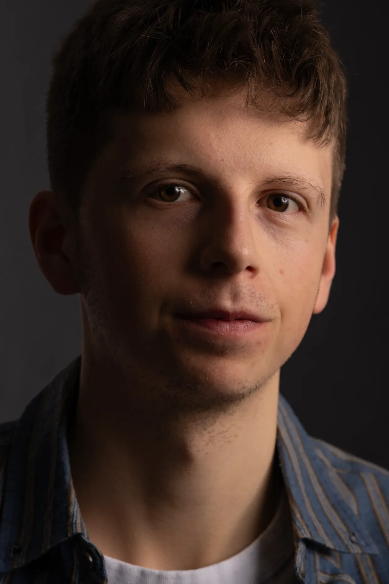 Low-Key-Porträt eines jungen Mannes vor dunklem Hintergrund, das Gesicht seitlich ausgeleuchtet